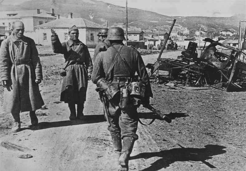 Немецкие солдаты идут мимо двоих пленных красноармейцев в Керчи. Апрель 1942 г.